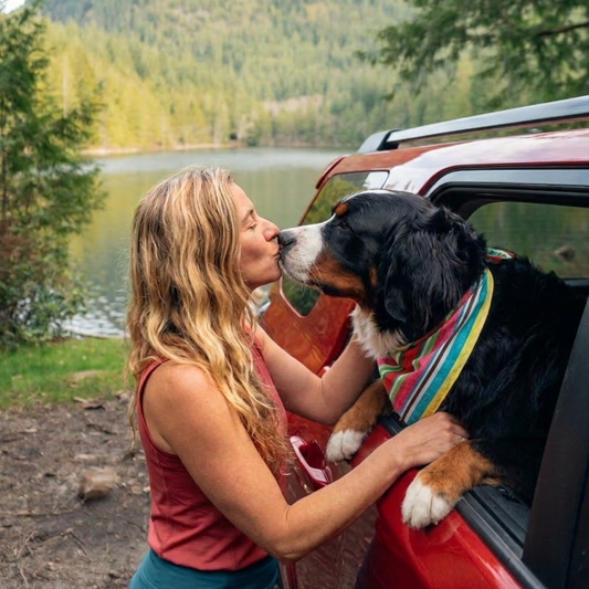 Woman kissing a dog by a lake with a car in the background