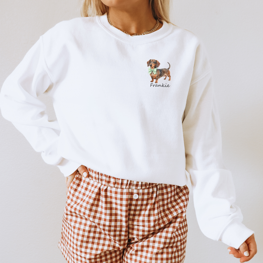 White sweatshirt with embroidered dog design and name, worn with brown checkered pants.