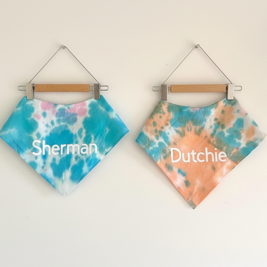 Two tie-dye bandanas hanging on wooden hangers with 'Sherman' and 'Dutchie' printed on them.