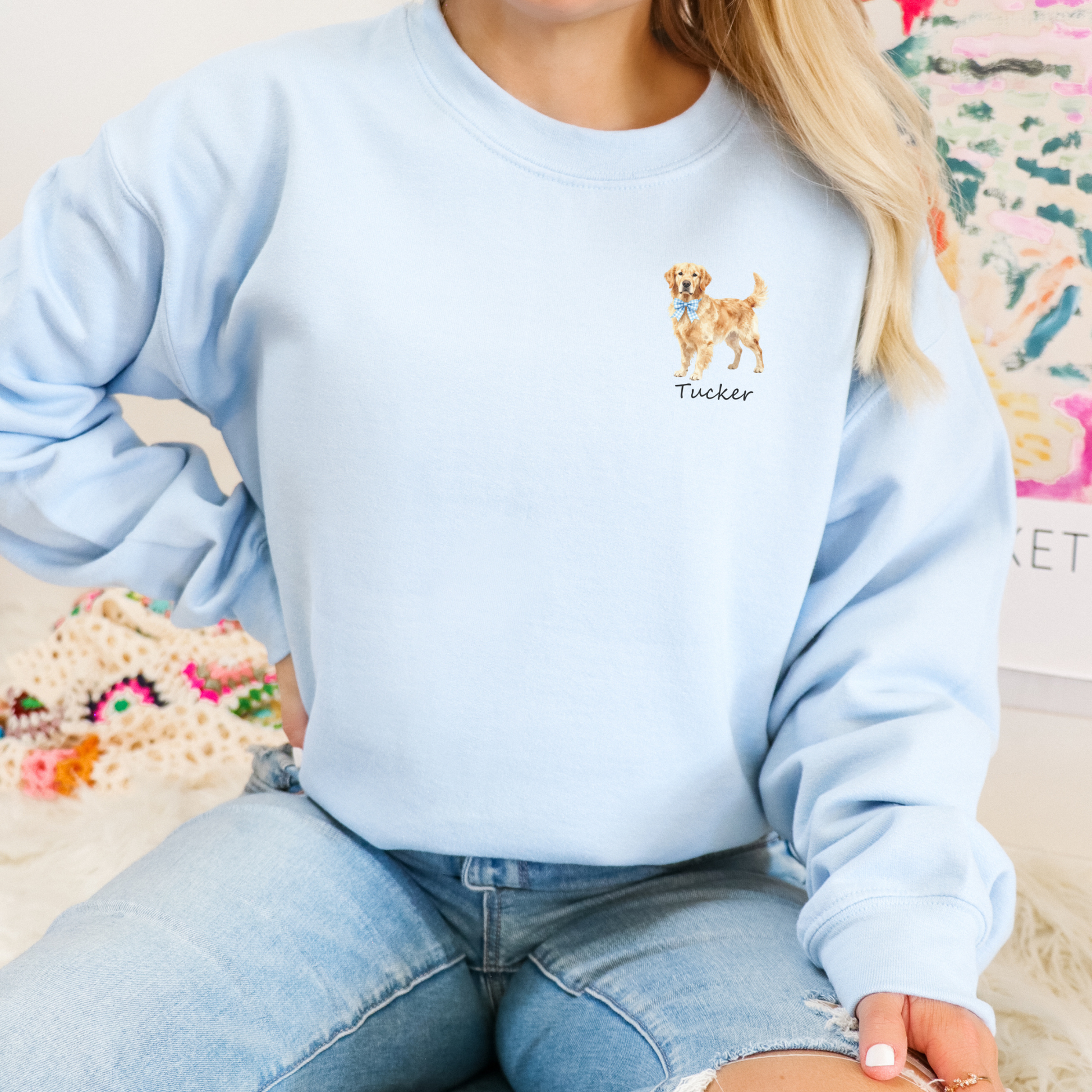 Light blue sweatshirt with embroidered dog design and name 'Tucker' worn by a person.