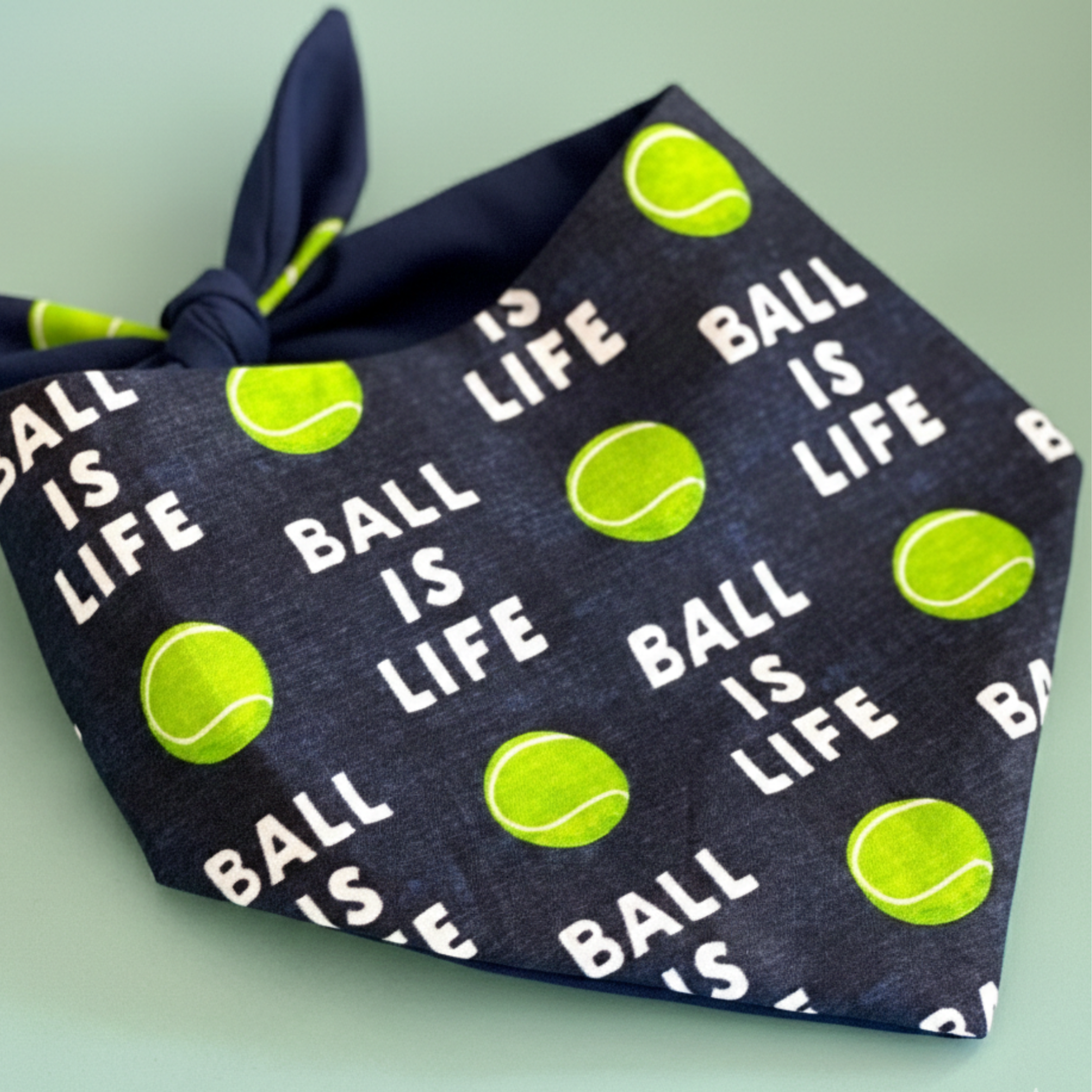 Navy bandana with tennis ball and 'Ball is Life' text pattern on a light green background