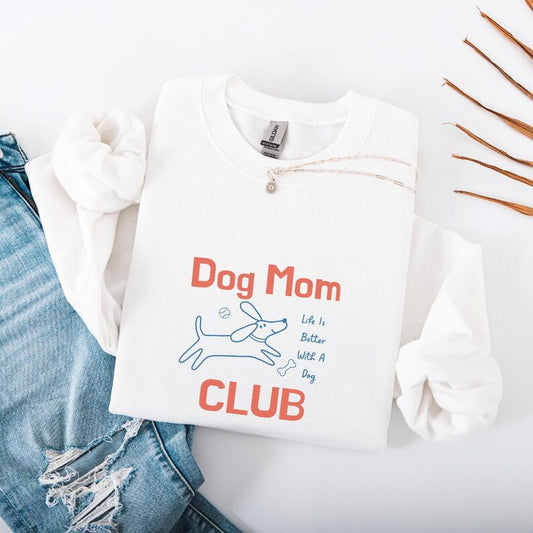 White sweatshirt with 'Dog Mom Club' text and graphics on a light gray background